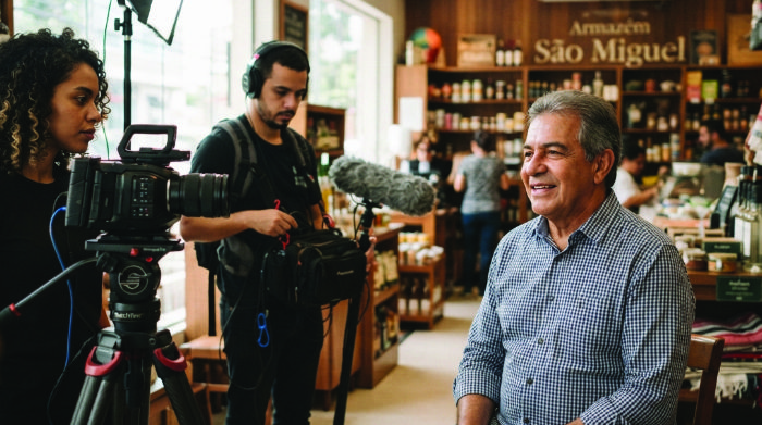 Vídeo institucional sendo produzido — equipe filmando dono de negócio tradicional com equipamento profissional